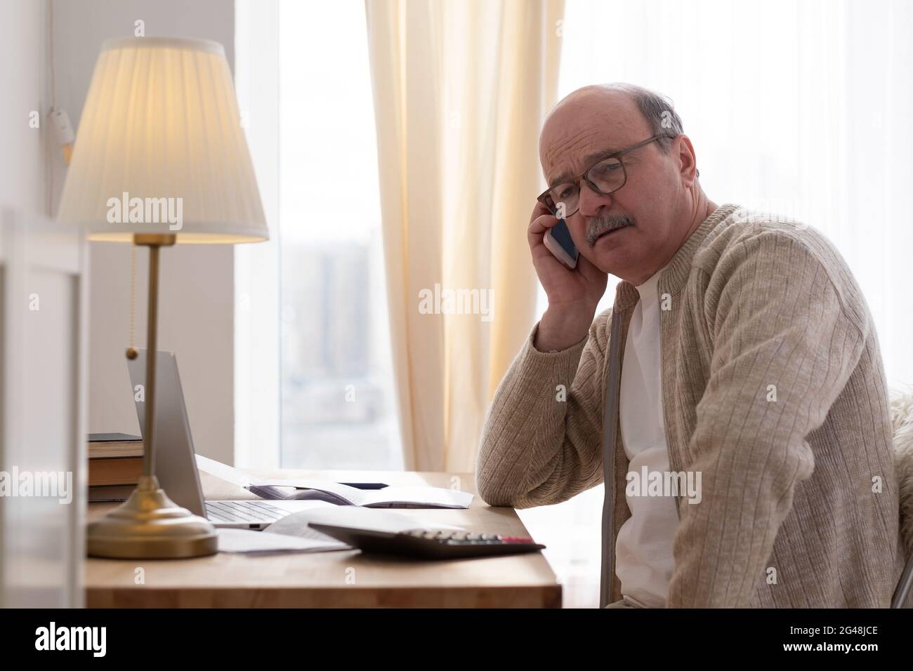 Senior man talking on phone sitting at table at home Stock Photo