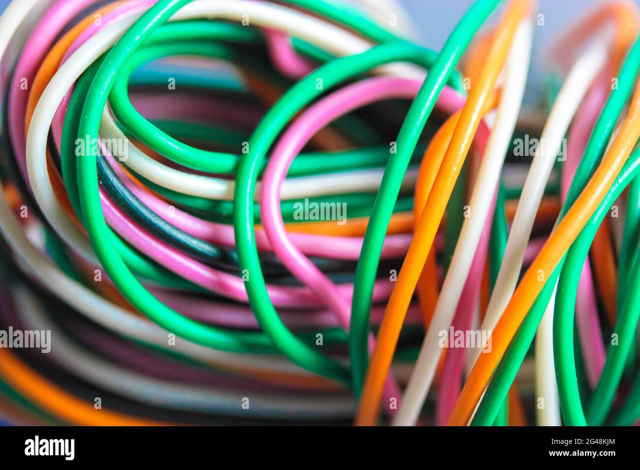 A bundle of multicolored electrical, car, computer, telephone wires twisted together background. Orange, green, pink, white cables on grey background Stock Photo