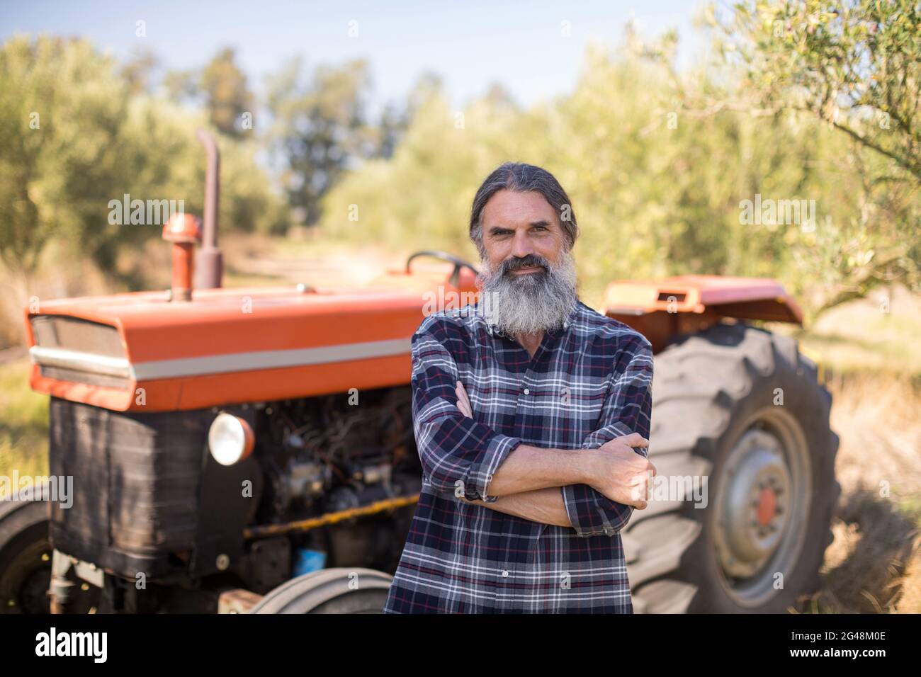 Portrait of happy man standing with arms crossed against tractor Stock ...
