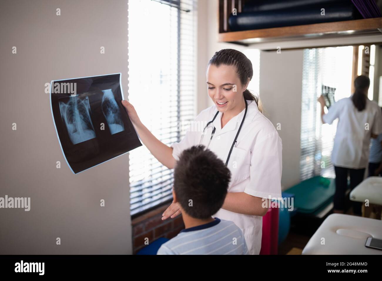 Female therapist holding x-ray while looking at boy Stock Photo