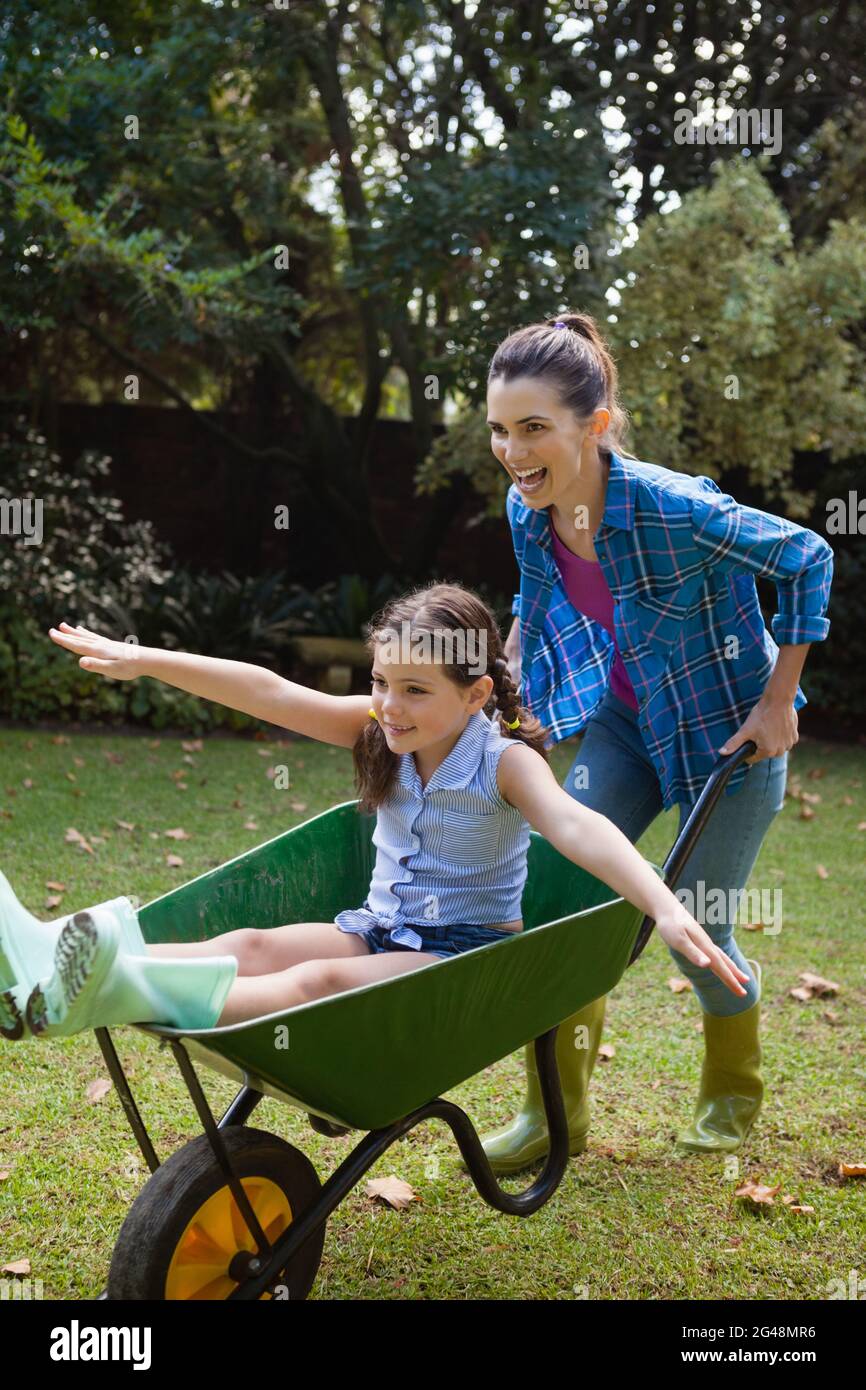 Happy woman pushing daughter sitting in wheelbarrow Stock Photo - Alamy