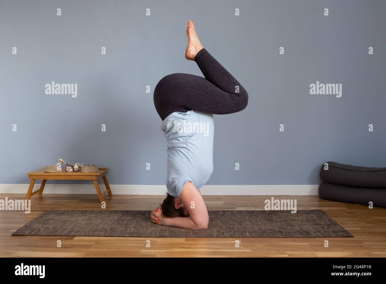 Pregnant woman doing exercises standing in a yoga pose headstand on her head. Stock Photo