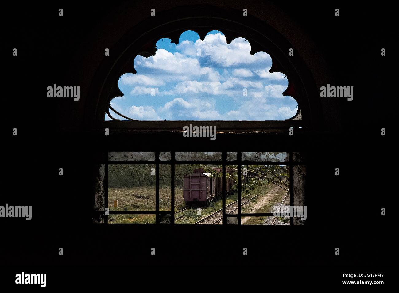 Train on the tracks under cloudy blue sky as seen through an arched ...