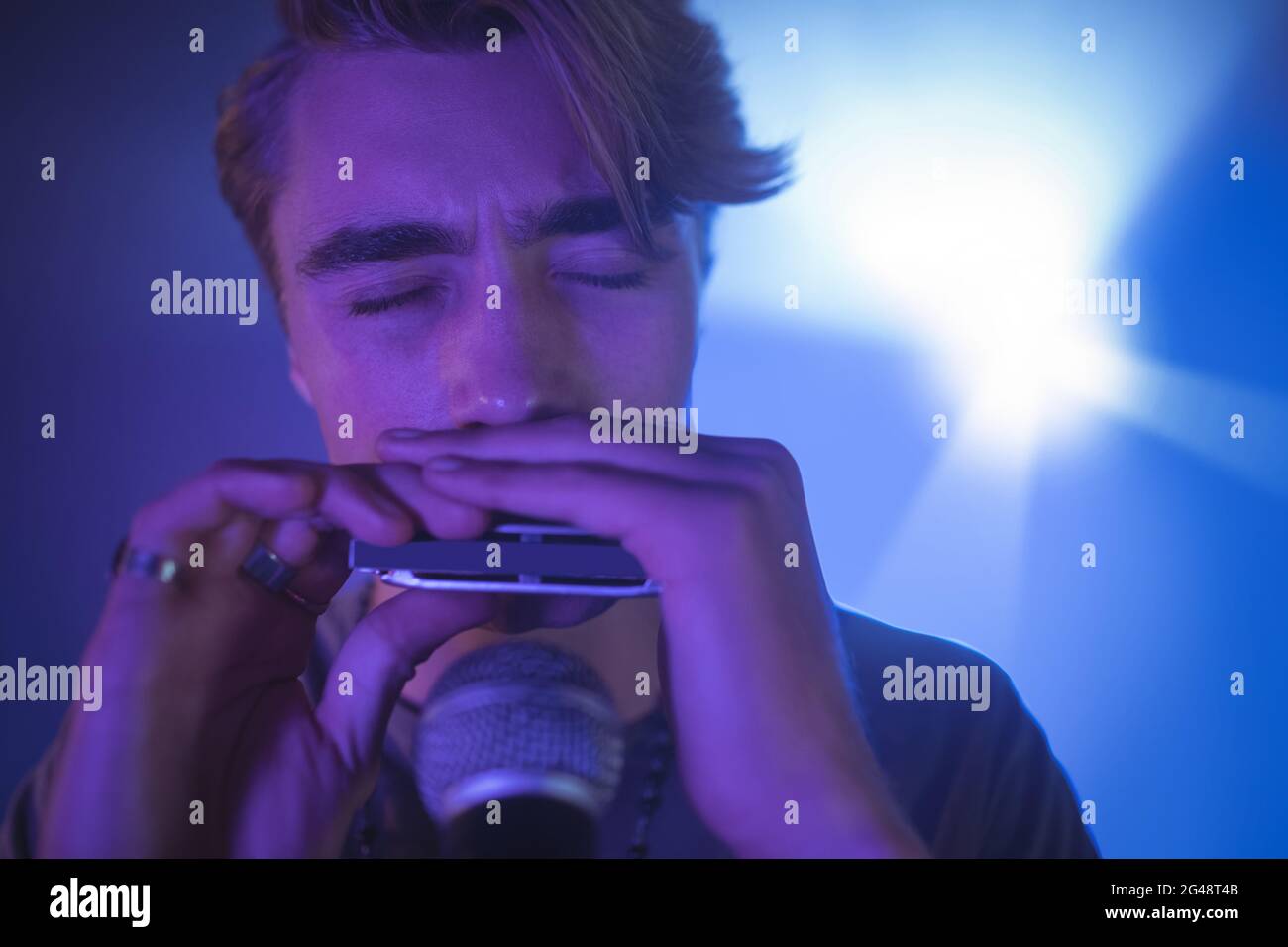 Male musician playing mouth organ in illuminated Stock Photo