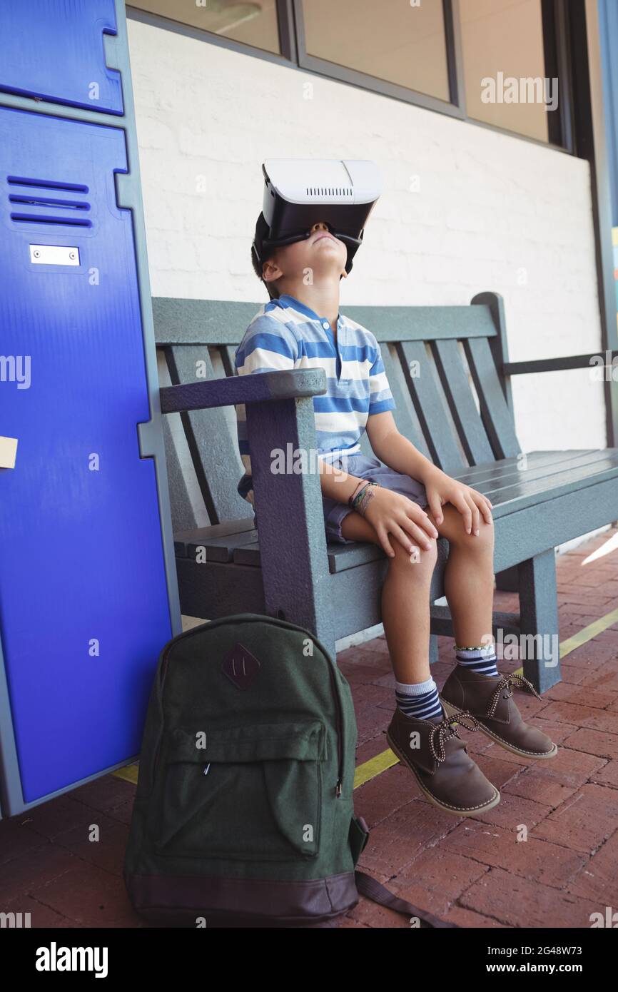 Boy using virtual reality glasses while sitting on bench Stock Photo