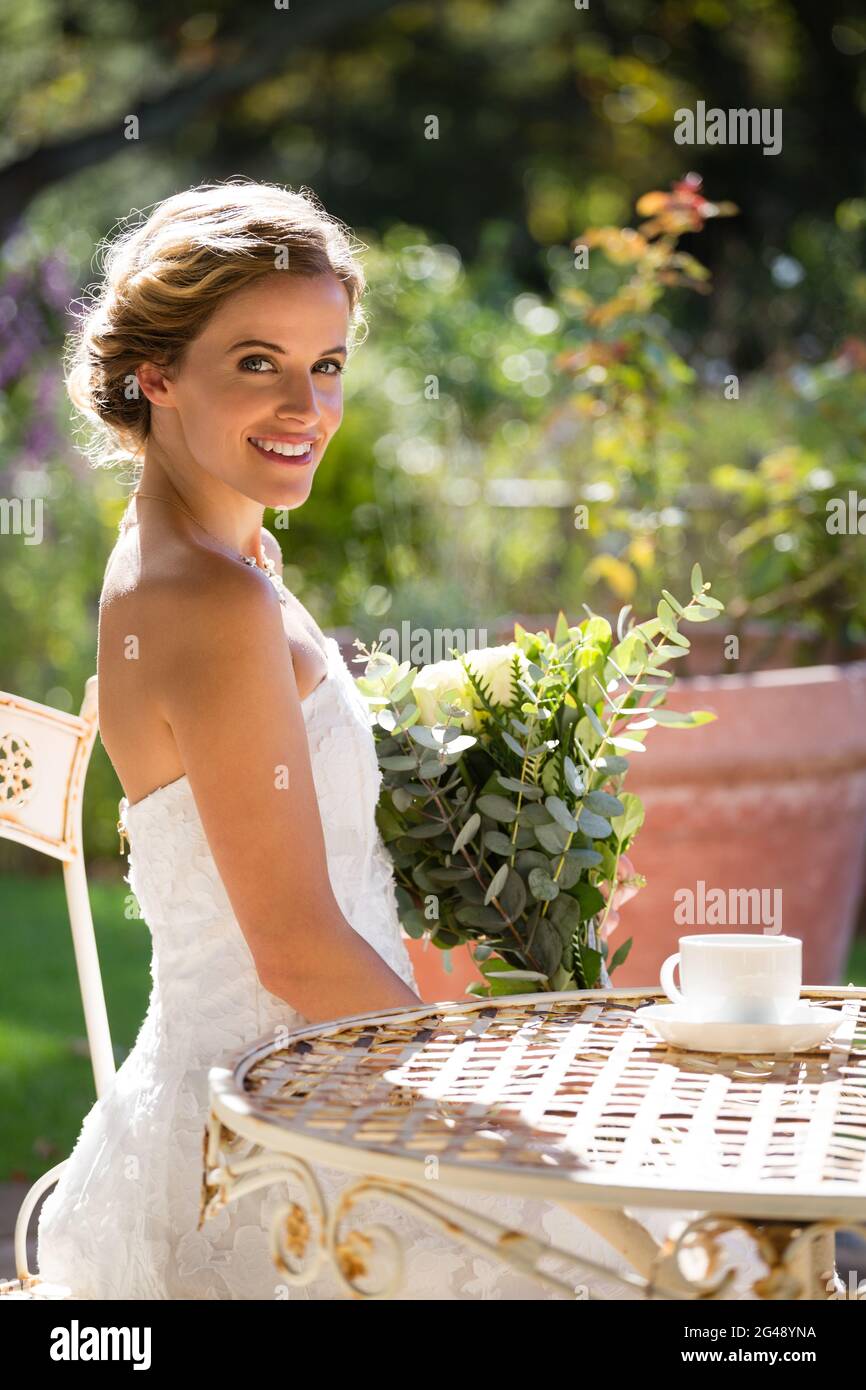 Portrait of smiling bride holding bouquet while sitting on chair Stock ...