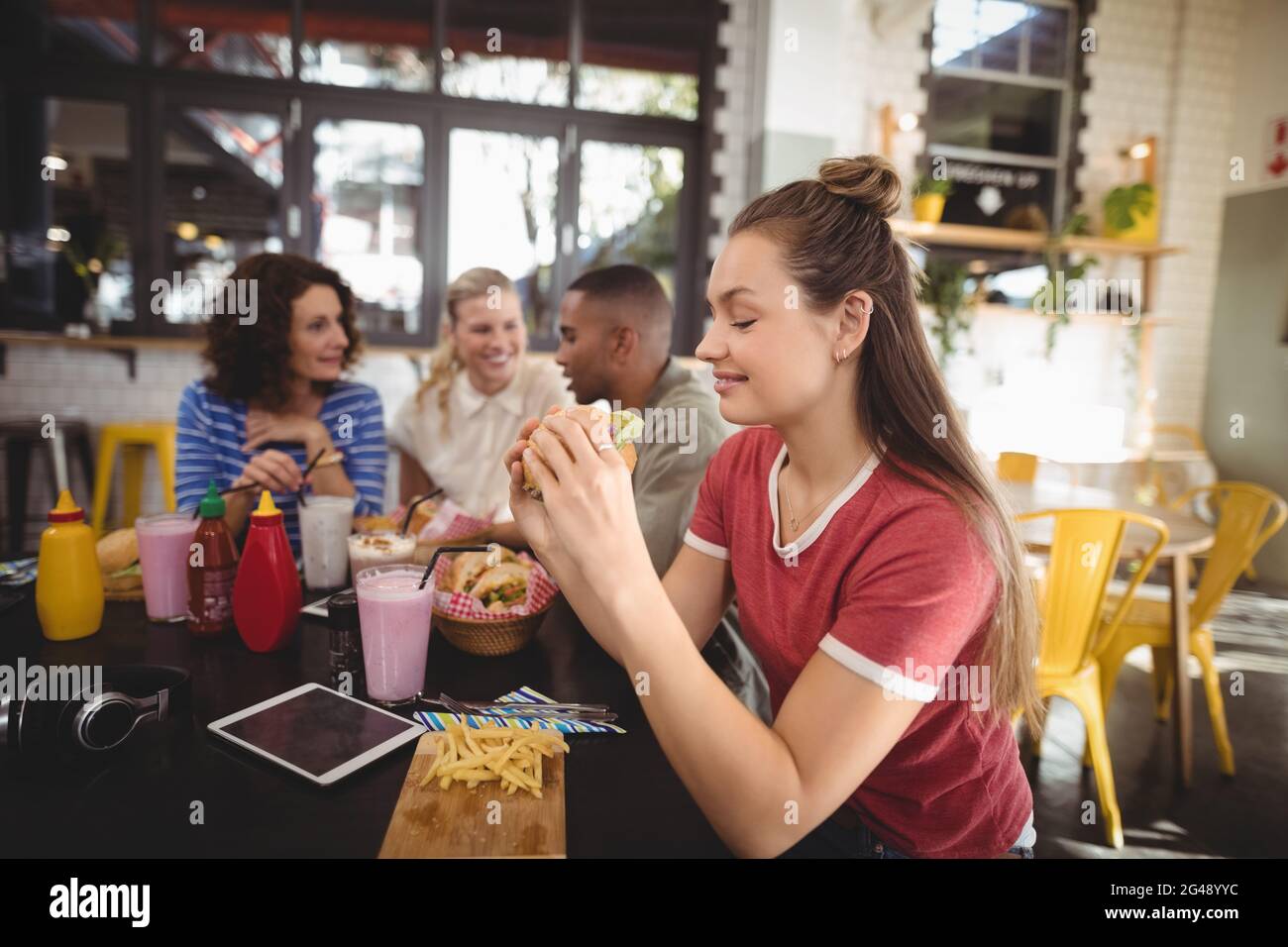 Beautiful young woman eating burger while sitting at coffee shop Stock Photo