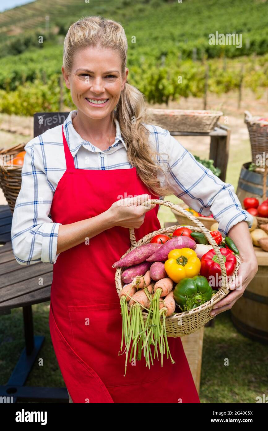 Happy woman holding a basket of fresh vegetables at stall Stock Photo ...