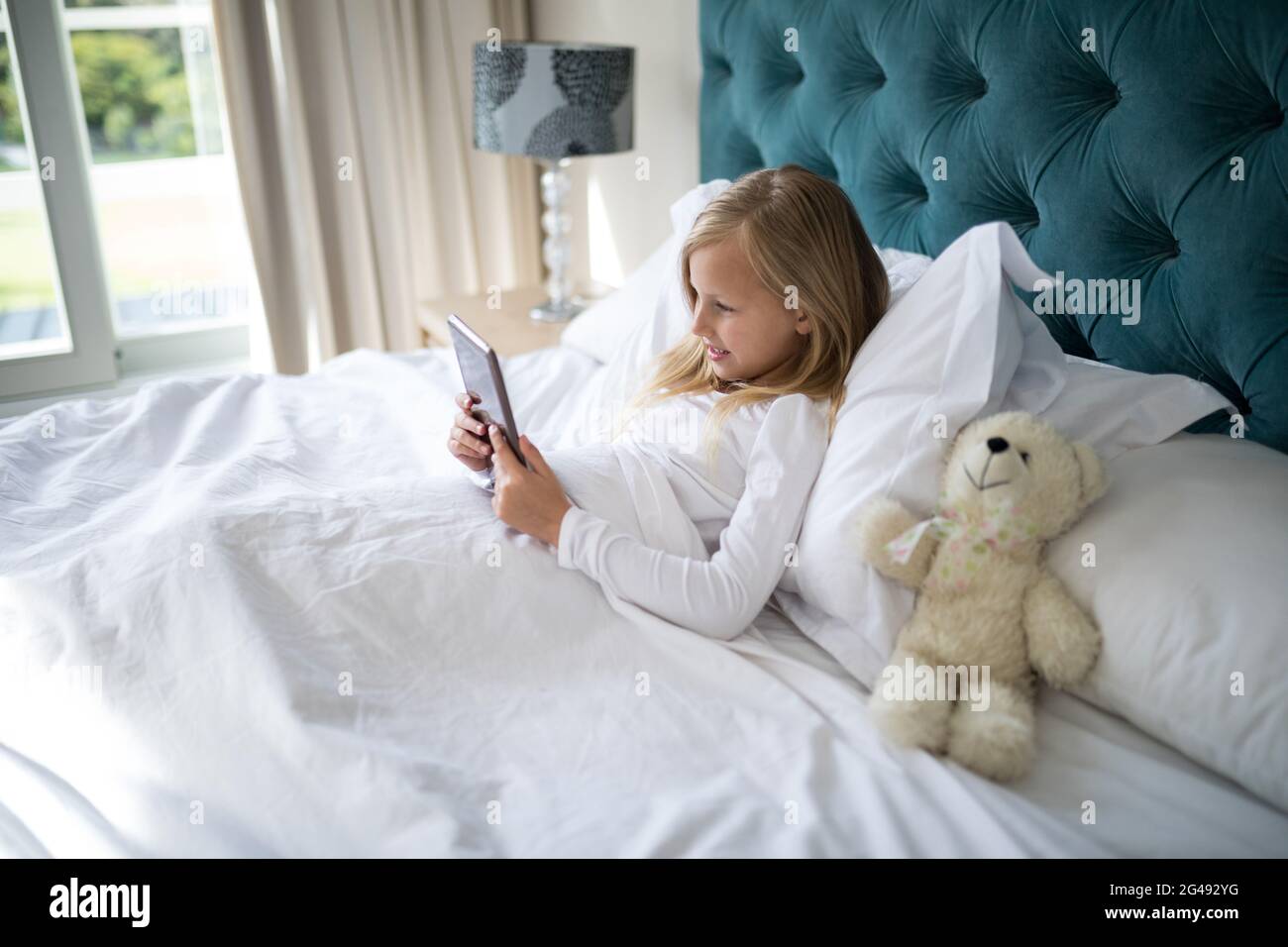 Girl using digital tablet while lying on bed Stock Photo - Alamy