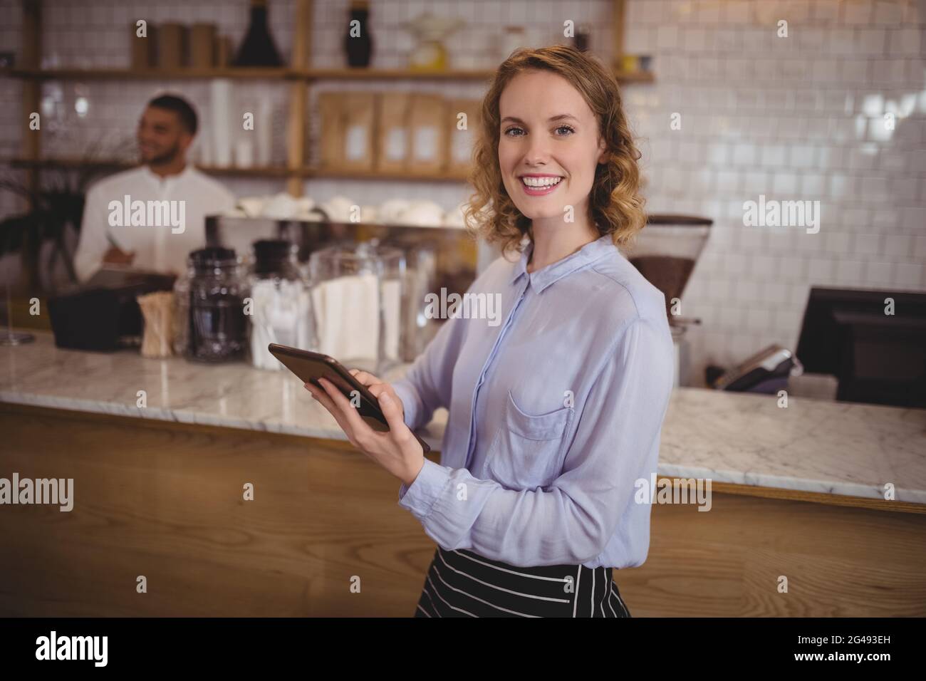 Smiling young waitress using digital tablet while standing by counter Stock Photo