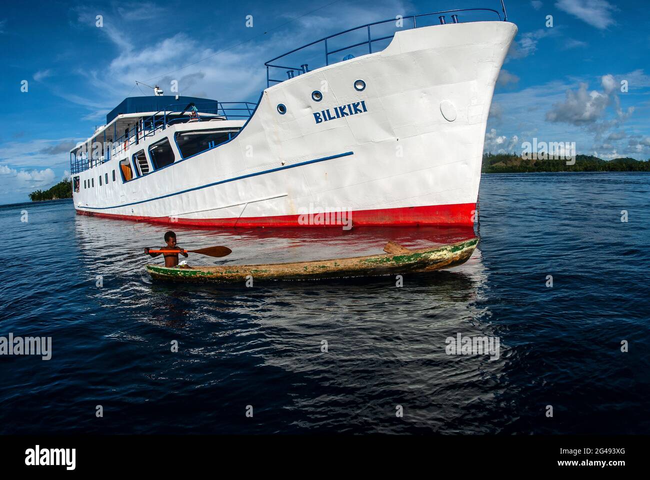 Young Solomon Islander boy in dugout canoe near ship, Solomon Islands Stock Photo