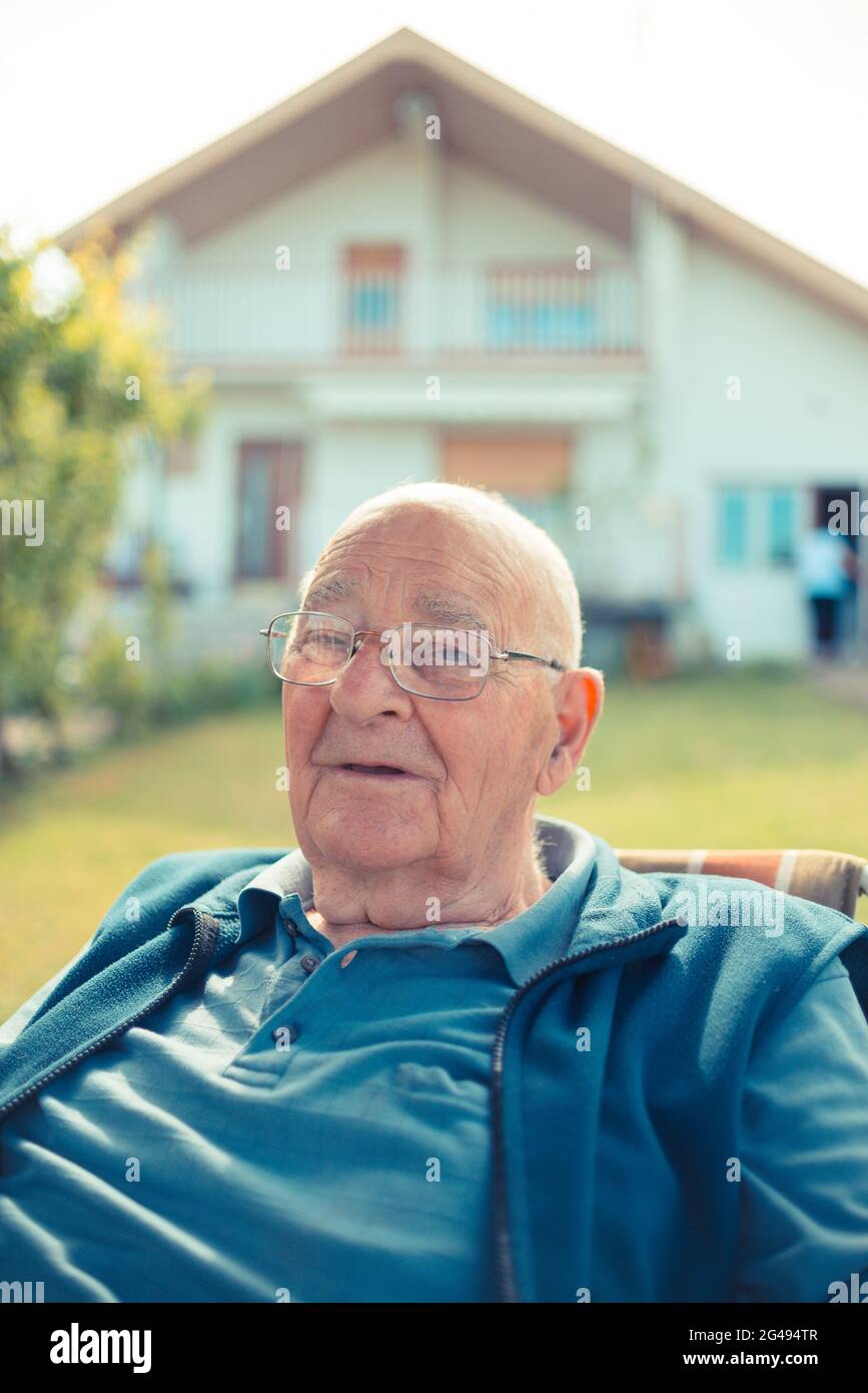 Senior man relaxing sitting in front of his house Stock Photo