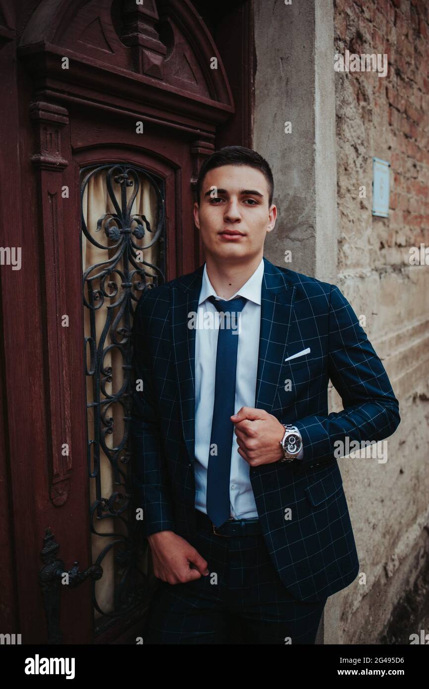 Caucasian young businessman in a suit and tie posing against the door ...