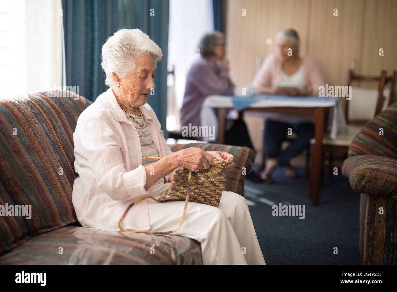 Side view of senior woman knitting while sitting on sofa Stock Photo ...