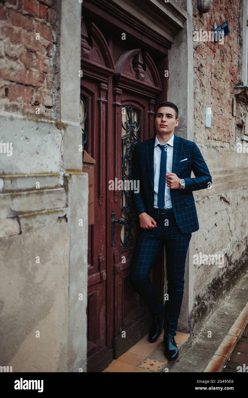 Caucasian young businessman in a suit and tie posing against the door ...