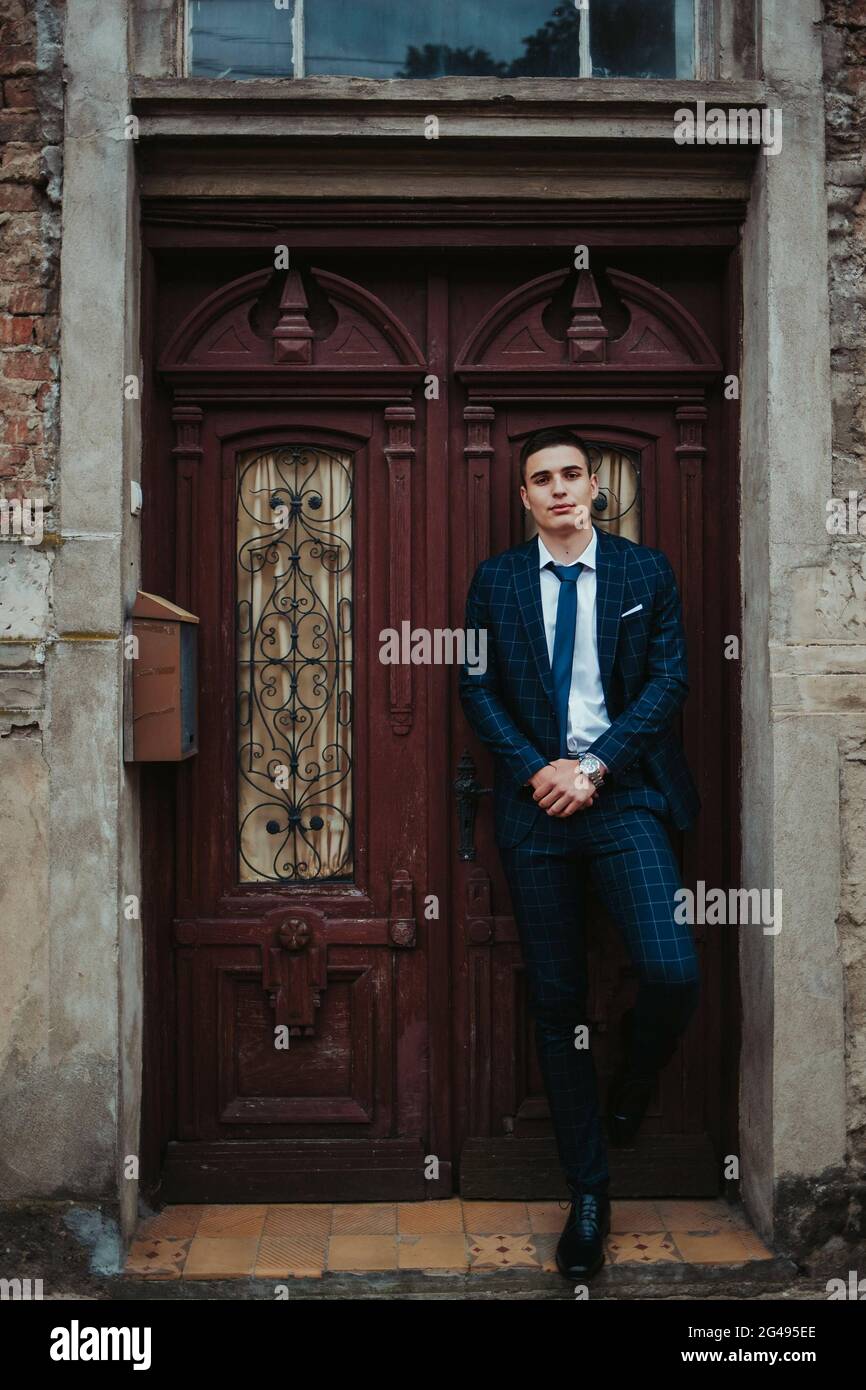 Caucasian young businessman in a suit and tie posing against the door ...