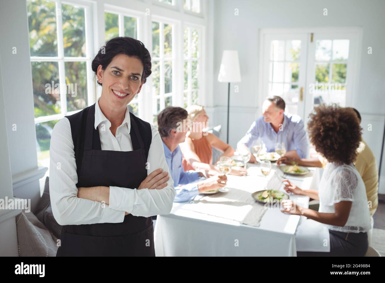 Smiling waitress standing with arms crossed Stock Photo - Alamy