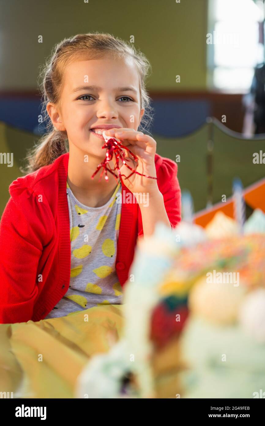 Cute girl blowing party horn during birthday party Stock Photo - Alamy