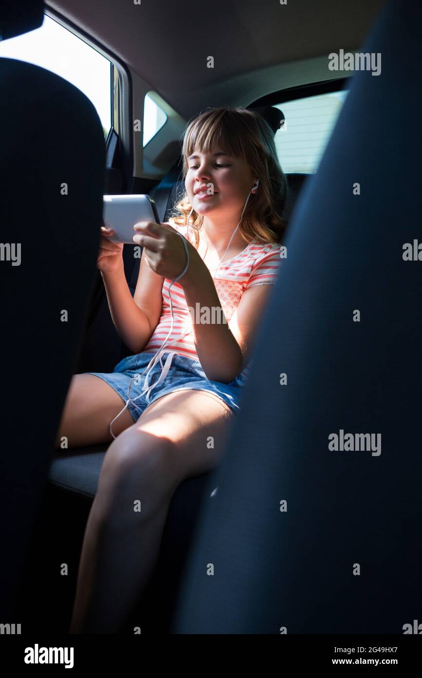 Teenage girl in headphones using mobile phone in the back seat of car Stock Photo Alamy