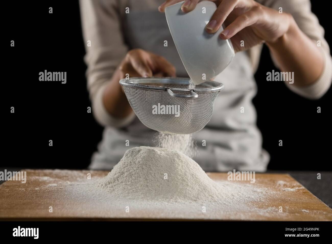 Woman sieving flour from the bowl on the wooden board Stock Photo Alamy