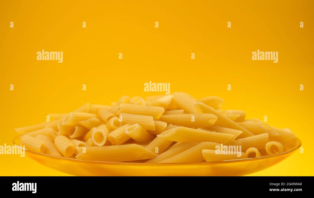 Raw italian penne rigate pasta on yellow color background with copy space Stock Photo