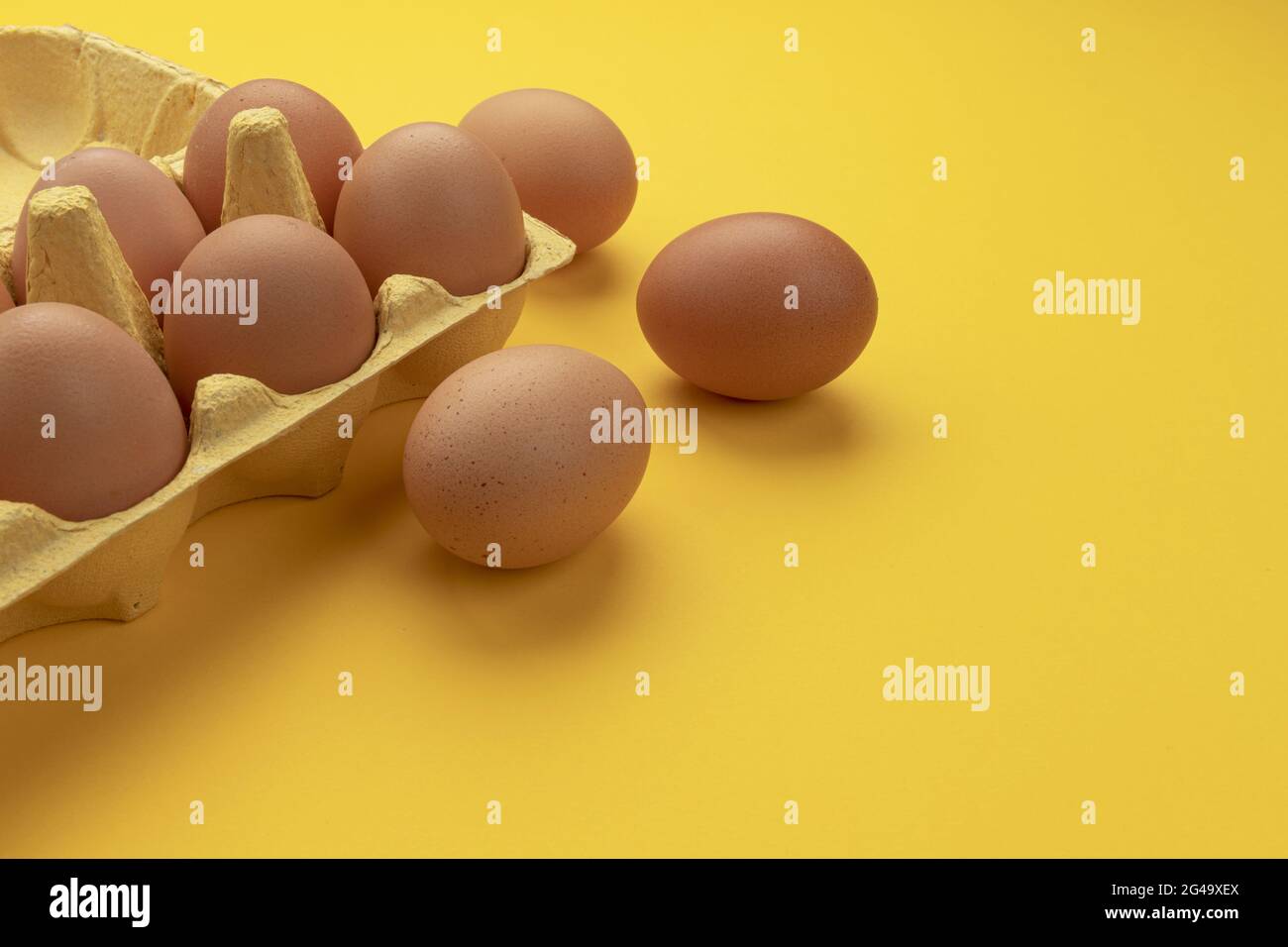 Brown chicken eggs in cardboard box on yellow background Stock Photo