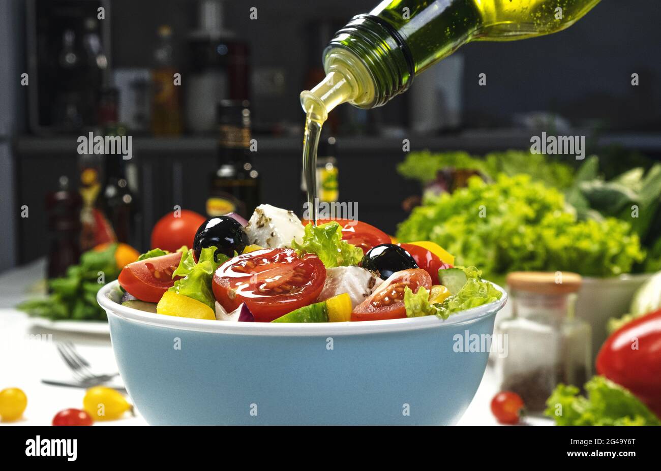 Pouring Olive oil on fresh Vegetable salad, Greek salad on white table Stock Photo