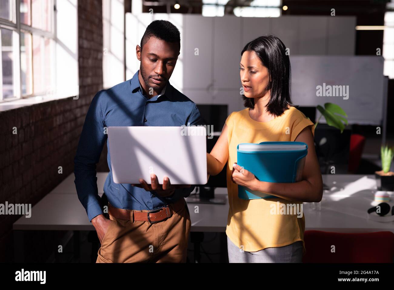 Serious diverse male and female colleague standing in office discussing ...
