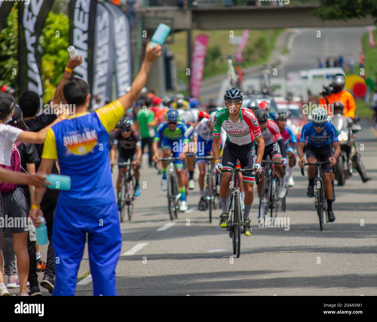Cyclists passing by the refreshment line of the Liga de Boyaca team during the SUB-23 Qualifiers Colombian National Road Race Bicycle Championship in Pereira, Colombia on June 19, 2021. Stock Photo