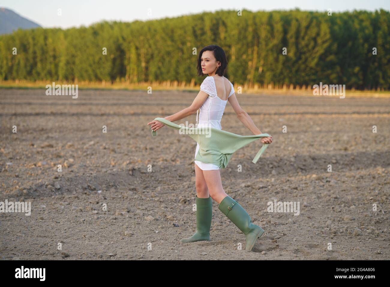 Asian woman, walking in the countryside, wearing a white dress and green wellies. Stock Photo