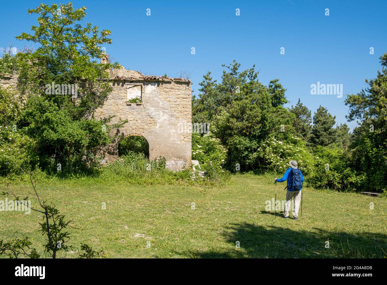 Man with backpack admiring  the ruins of old house in the countryside. Podere Montebello, Modigliana, Forlì, Emilia Romagna, Italy, Europe. Stock Photo