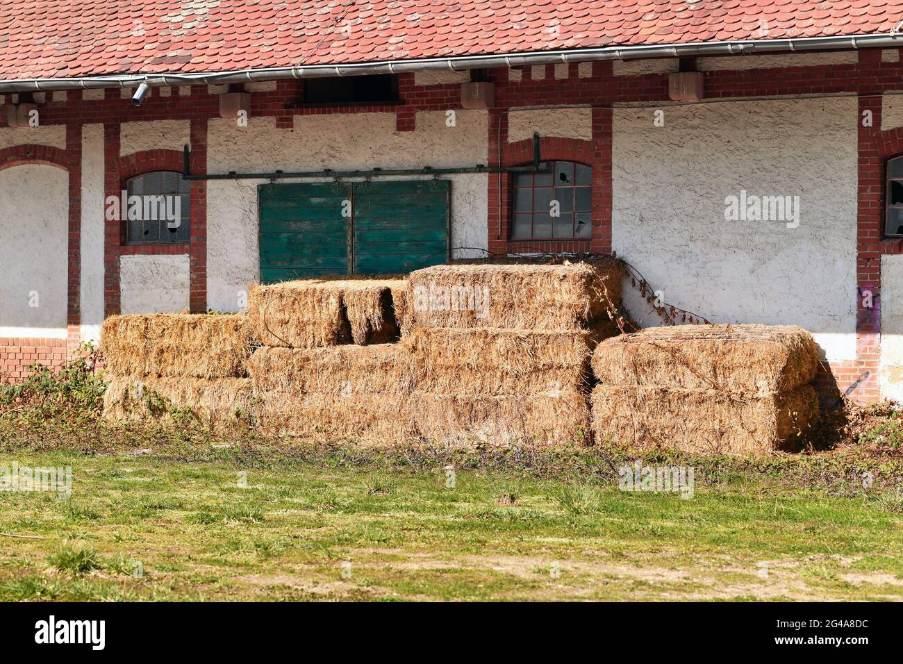 Old rectangular hay bales stored in front of old abandoned farm building Stock Photo
