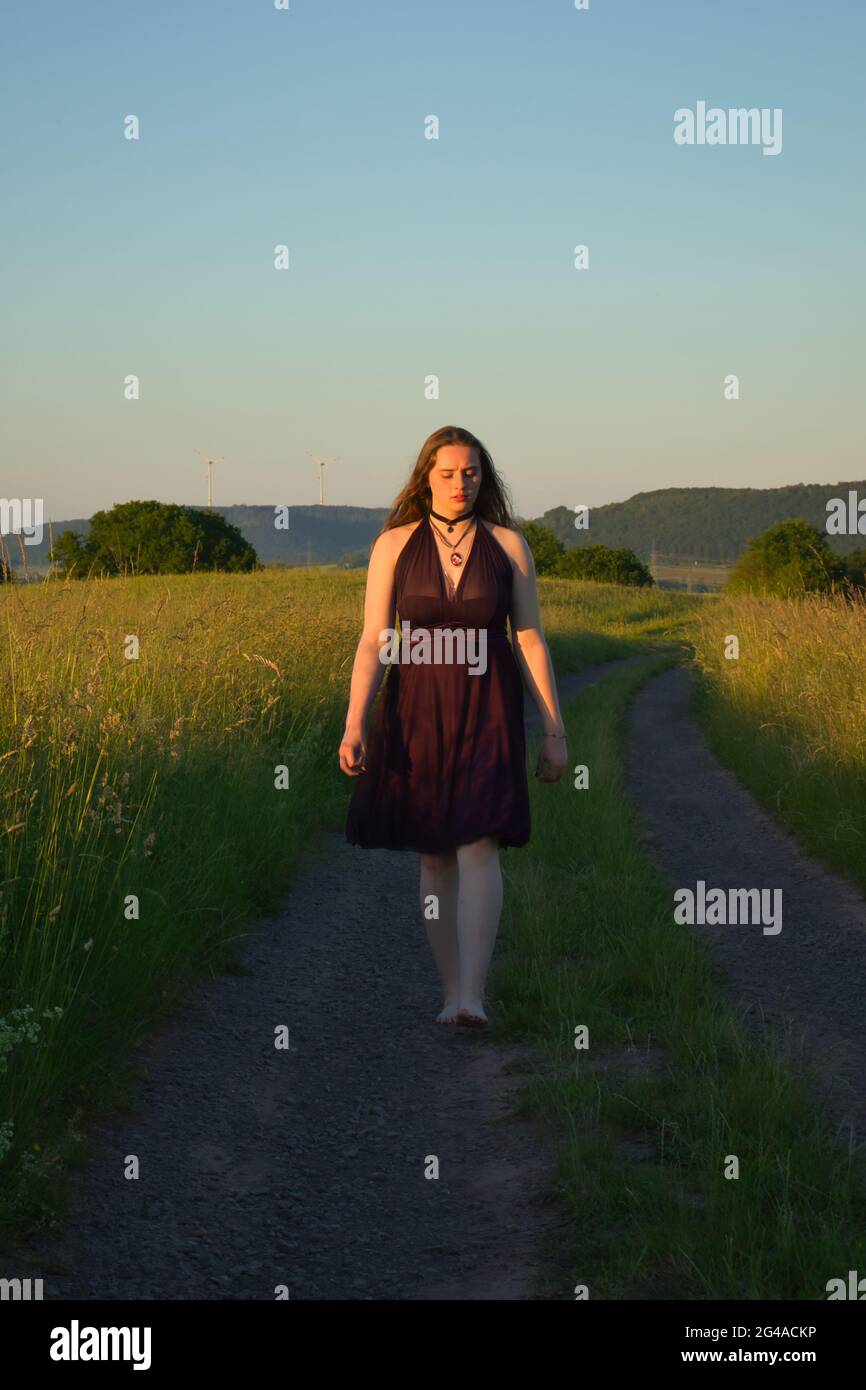 Teenage girl with long hair walking on a dirt road in rural Germany on a warm spring night. Stock Photo