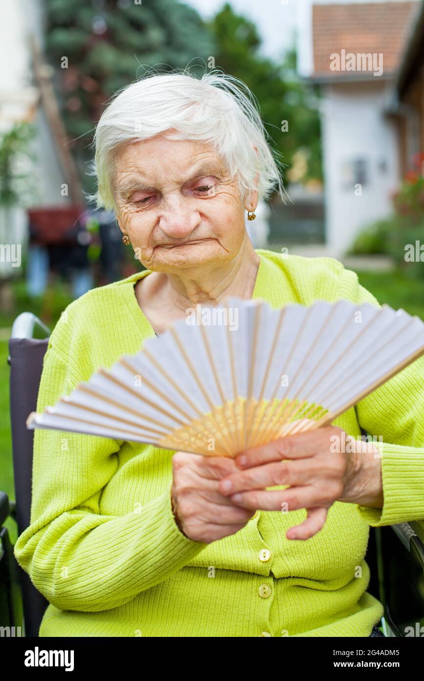 Senior woman holding waving fan on a hot summer day Stock Photo