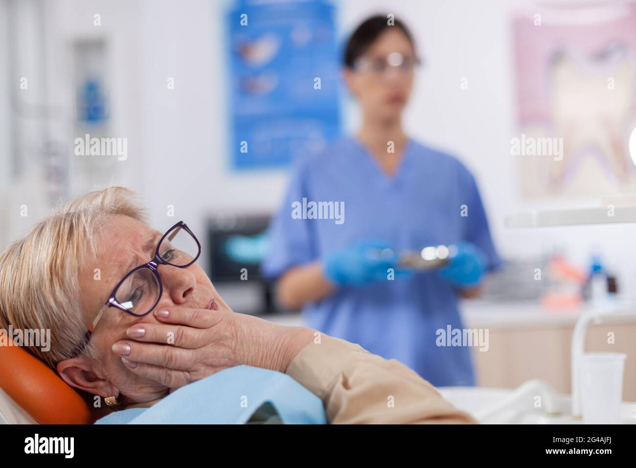 Elderly patient in pain at dentist clinic waiting diagnosis from doctor in medical office. Senior woman in healthcare hospital accusing and complaining about tooth. Stock Photo