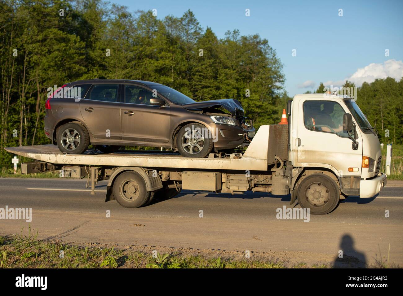 A tow truck is driving a car after an accident. Car transportation on a cargo platform. The loader takes away the emergency vehicle. Stock Photo