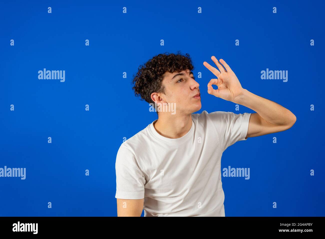 Attractive young man with curly hair making thumb sucking gesture isolated on blue studio background. Gesture concept Stock Photo