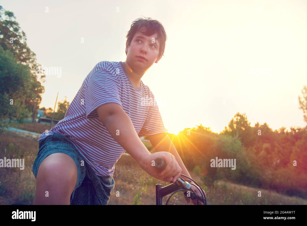 Happy boy posing in a bicycle outdoors at sunset Stock Photo