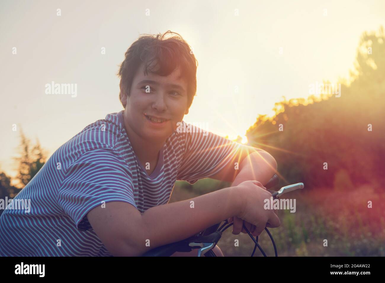 Happy boy posing in a bicycle outdoors at sunset Stock Photo