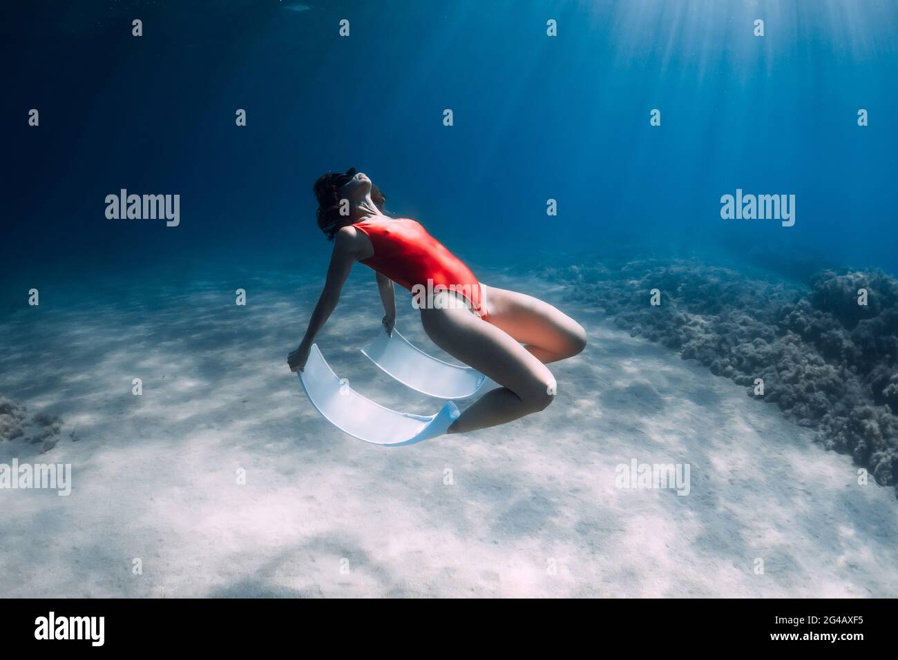 Freediver woman in swimsuit with white fins posing underwater over sand in transparent ocean. Stock Photo