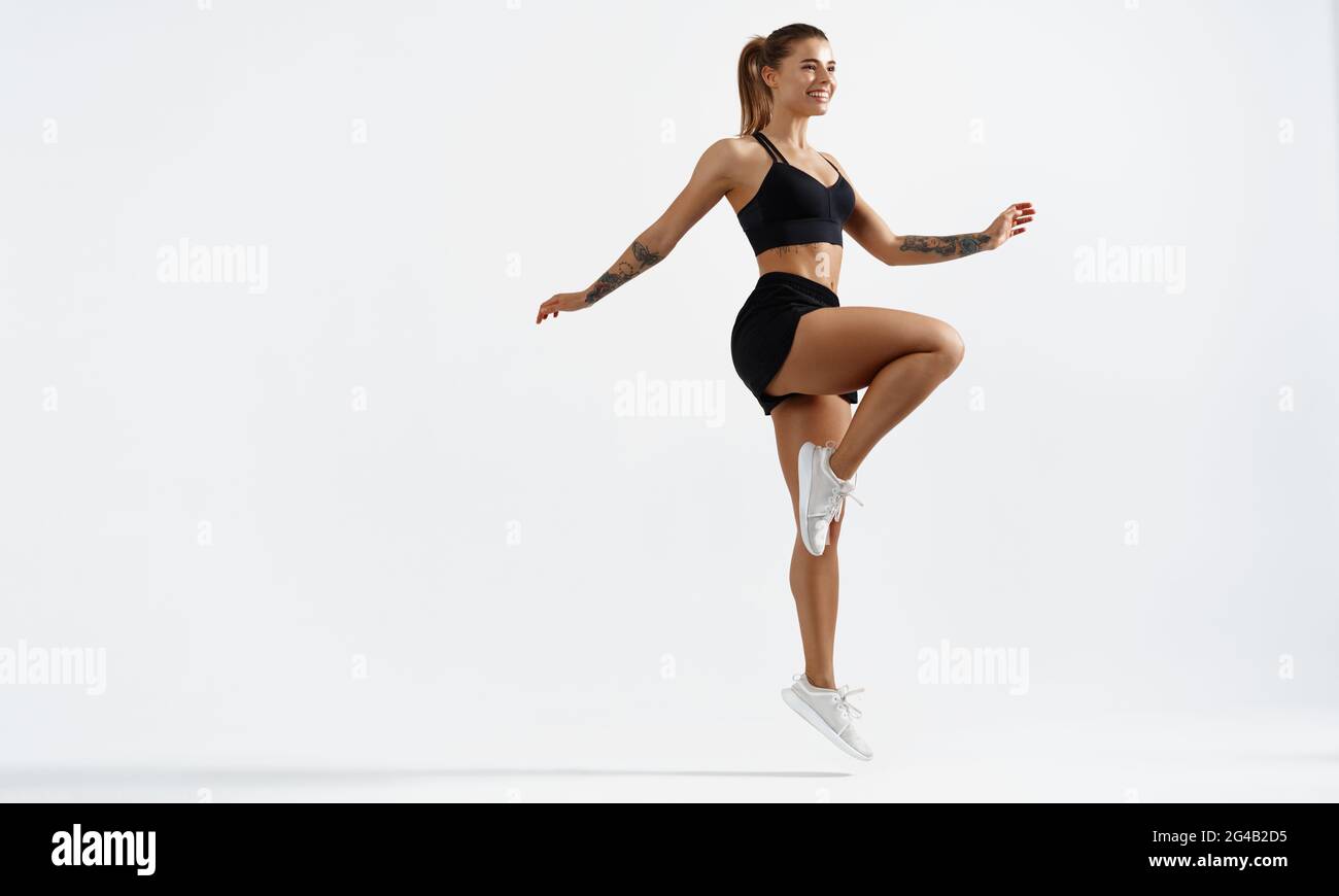 Fitness woman in sportswear doing stretching exercise isolated against white background. Female athlete raise, lifting leg, workout warm-up before Stock Photo