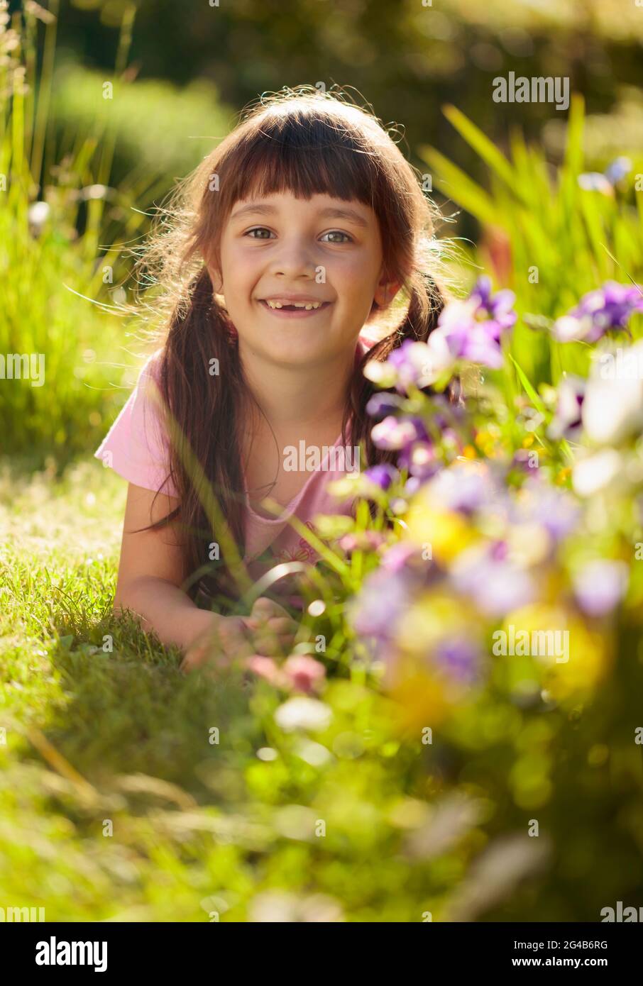 Happy little girl laying on a grass in the garden. Sunny summer day in ...