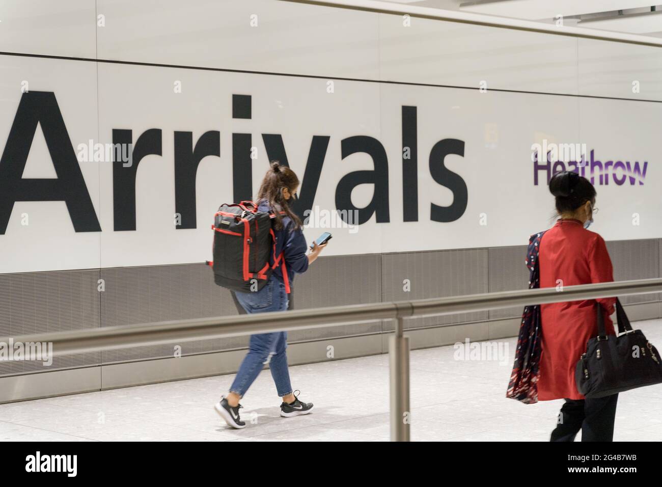 Travellers at international arrivals hall with rucksack and hand bags, looking at her mobile at London Heathrow Airport, England, UK Stock Photo