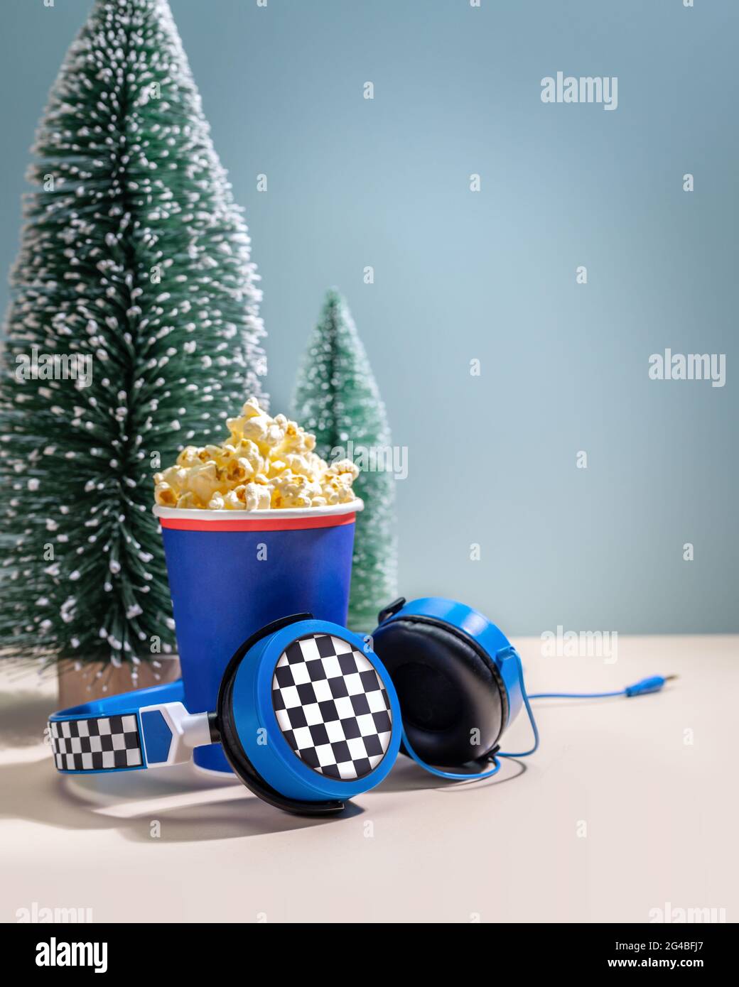 New Year holliday composition with disposable cup with popcorn, headphones and decorative christmas trees. Concept of playing games and watching movie Stock Photo