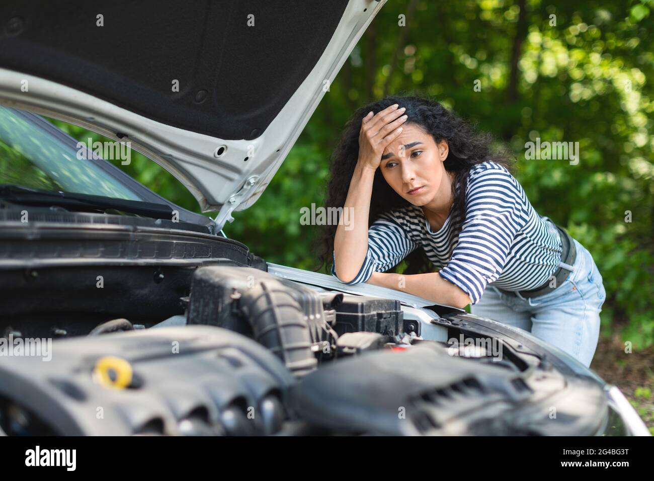 Sad brunette woman leaning on car hood, waiting for service Stock Photo