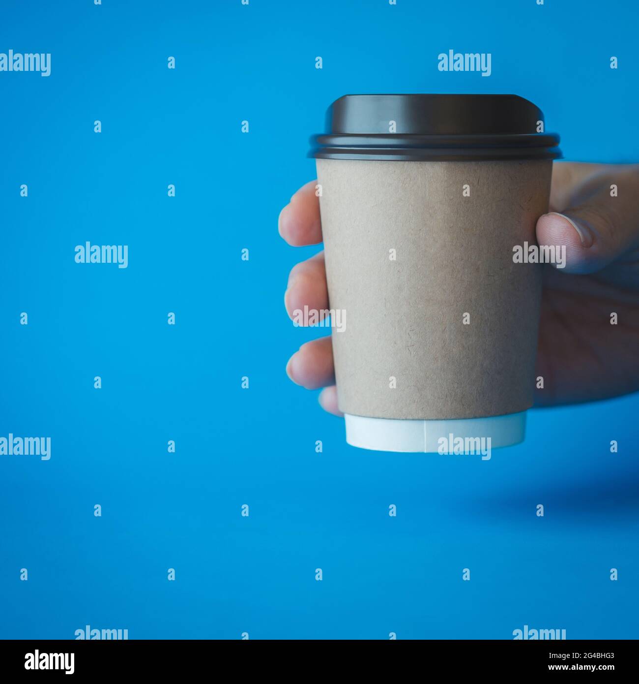 Close up of Man Hand Holding a Recycle Brown Paper Coffee Cup on a Blue Background, Mockup Template for Logo Design, Branding, Copy Space for Text. Stock Photo