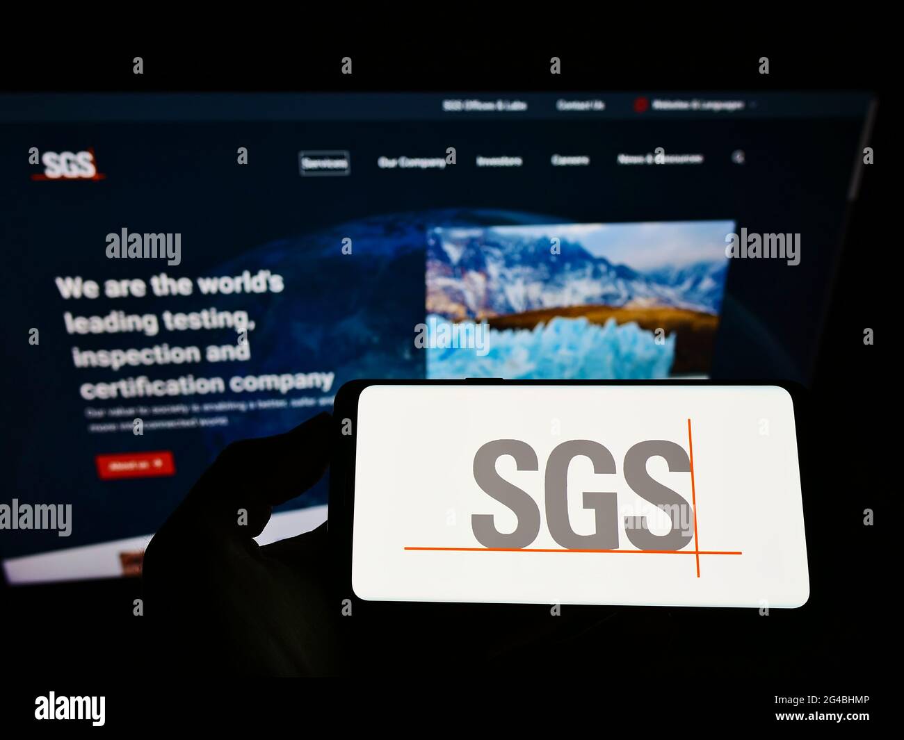 Person holding smartphone with logo of Swiss certification company SGS S.A. on screen in front of website. Focus on phone display. Stock Photo