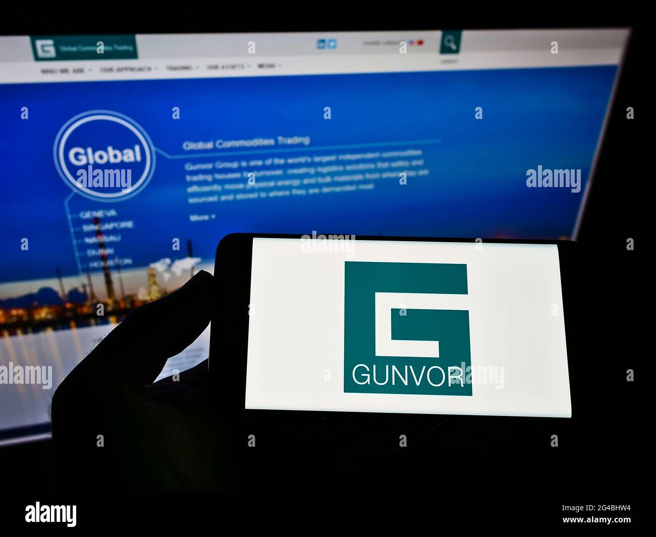 Person holding smartphone with logo of commodity trading company Gunvor Group Ltd on screen in front of website. Focus on phone display. Stock Photo