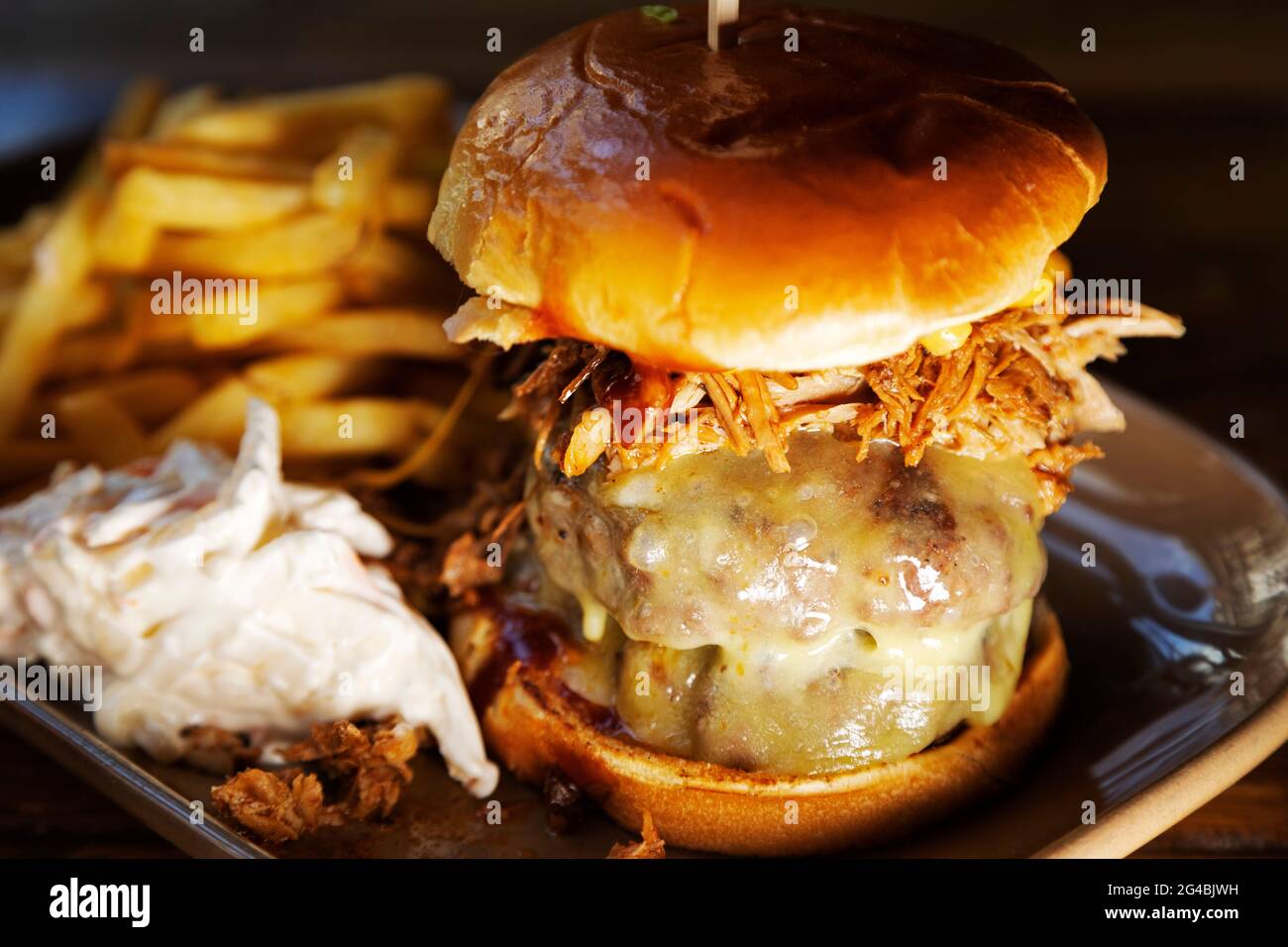 Burger in a brioche bun served with fried and 'slaw. The Burger is topped with melted cheese and shredded pulled pork. Stock Photo