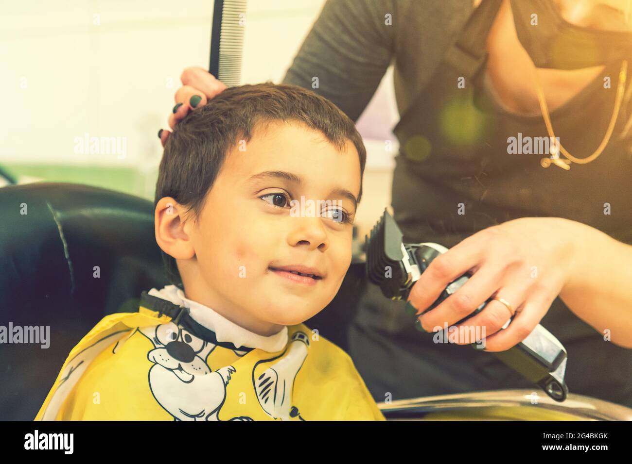 little boy having a haircut at hair salon..Children hairdresser with scissors and comb is cutting little boy. Contented cute preschooler boy getting Stock Photo